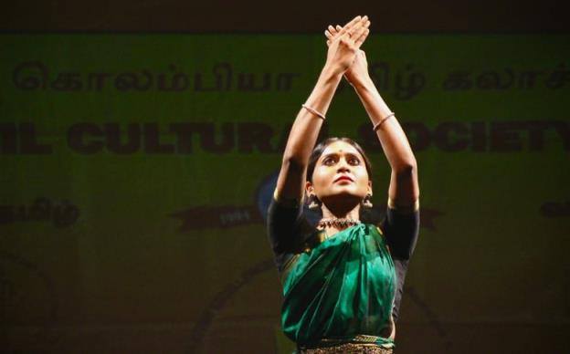 Young girls are dressed in green and blue South Asian clothing and adorned with traditio<em></em>nal jewellery. They are dancing at a performance for Tamil Heritage Month